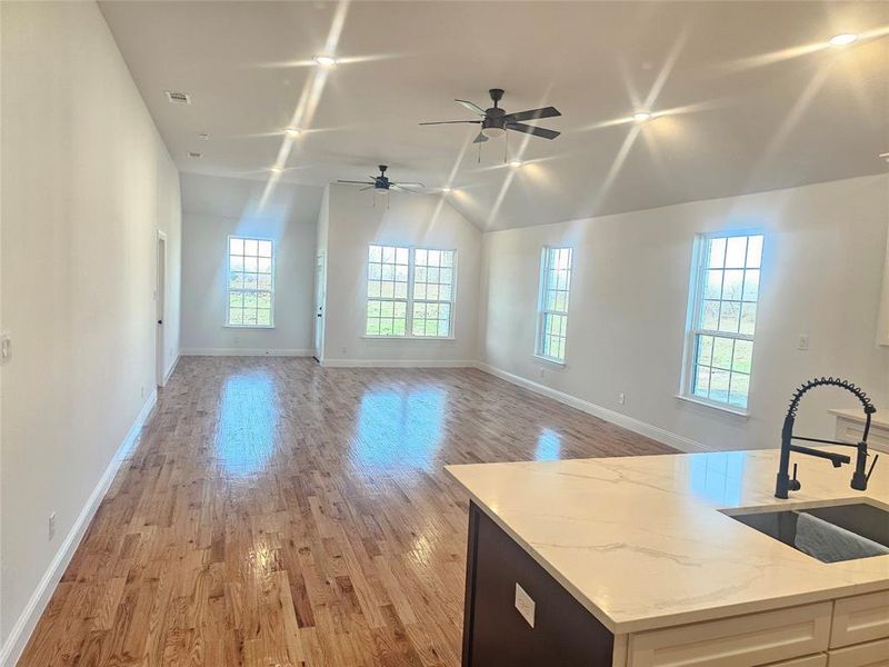 Kitchen with lofted ceiling, sink, light stone counters, white cabinetry, and light hardwood / wood-style floors