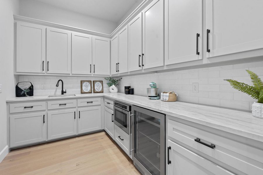 Kitchen featuring wine cooler, tasteful backsplash, white cabinets, and light stone countertops