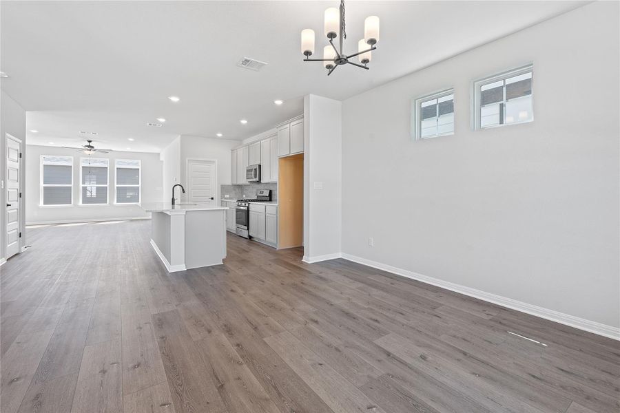 Kitchen with a chandelier, stainless steel appliances, open floor plan, decorative backsplash, and wood finished floors