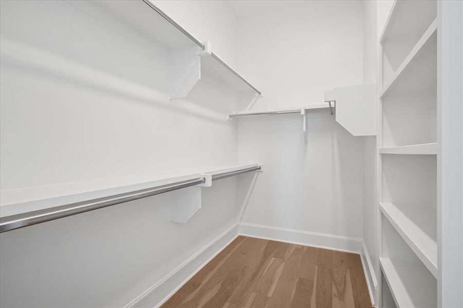Walk-in closet featuring built-in shelving, two hanging rods, and wood-finish flooring