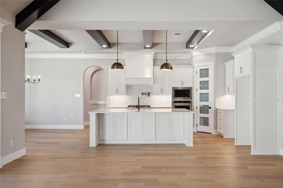 Kitchen with a center island with sink, decorative backsplash, decorative light fixtures, beam ceiling, and stainless steel appliances