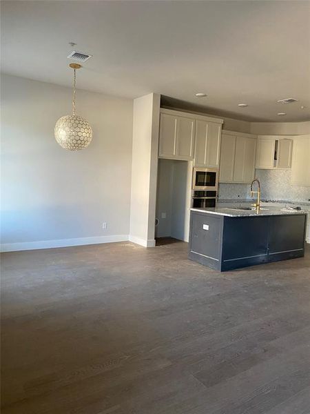 Kitchen with appliances with stainless steel finishes, pendant lighting, white cabinets, dark wood-type flooring, and decorative backsplash