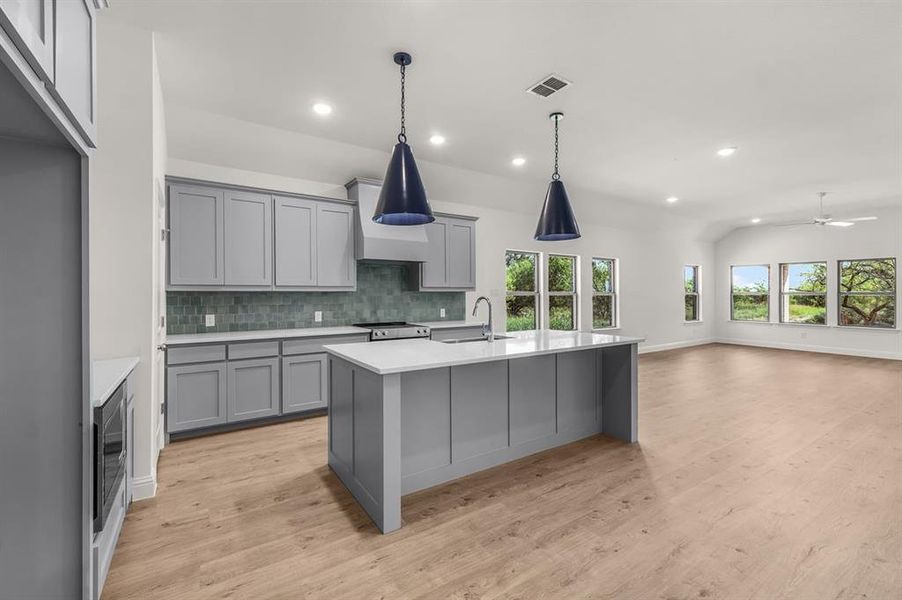 Kitchen featuring gray cabinetry, decorative backsplash, custom range hood, light floors, and recessed lighting