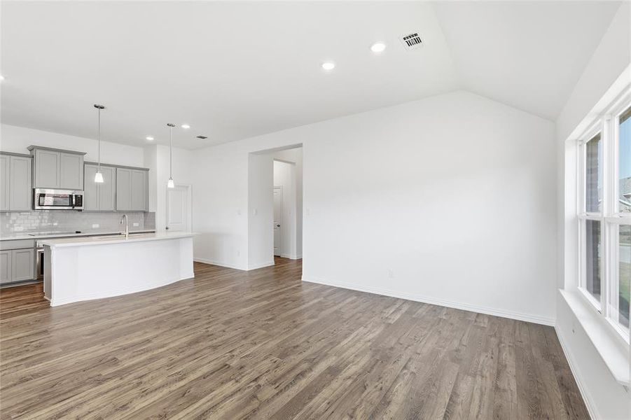 Spacious living area featuring wood-finish flooring, vaulted ceilings, and ample natural light from multi-pane windows