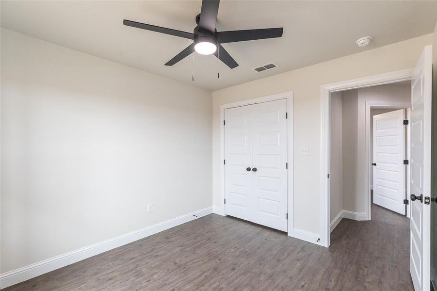 Room featuring wood-finish flooring, a contemporary black ceiling fan with integrated lighting, white baseboards, and a double-door closet with black hardware