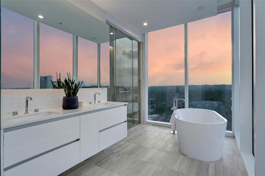 Soak in luxury with breathtaking sunset views from this spa-inspired primary bath. Featuring a freestanding soaking tub,  an expansive double vanity with sleek modern cabinetry, and a glass-enclosed two-person walk-in shower, this serene retreat combines elegance with panoramic Hill Country vistas (Photo from previous model Residence No. 2104 on lower level)