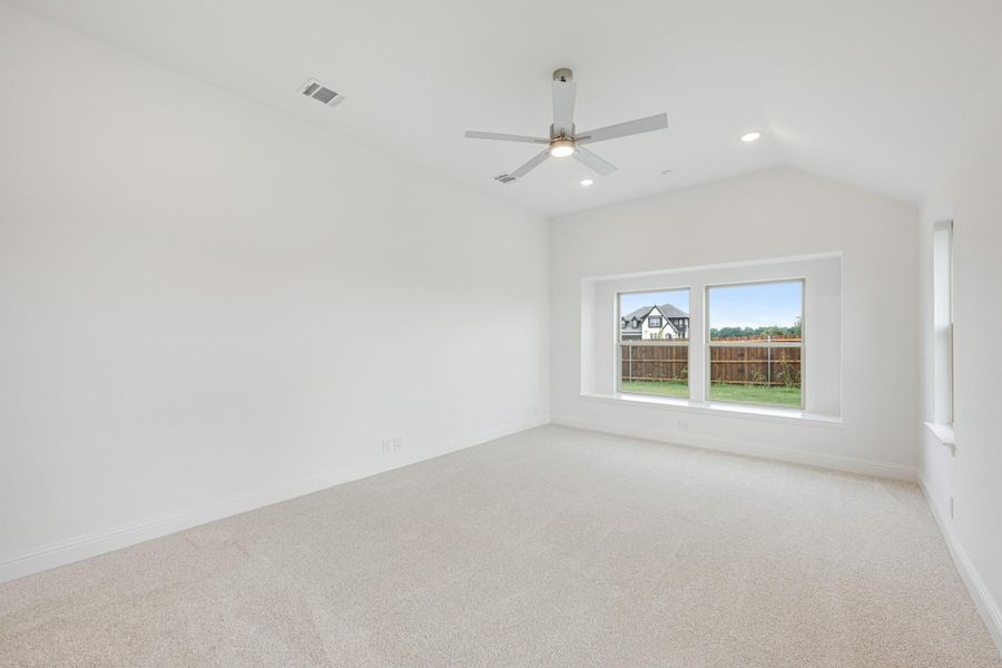 Empty bedroom with vaulted ceiling, ceiling fan, carpet flooring, and a window overlooking a backyard fence. Empty bedroom with vaulted ceiling, ceiling fan, carpet flooring, and a window overlooking a backyard fence.