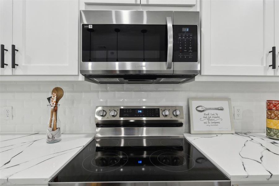 Kitchen with appliances with stainless steel finishes, tasteful backsplash, light stone counters, and white cabinetry