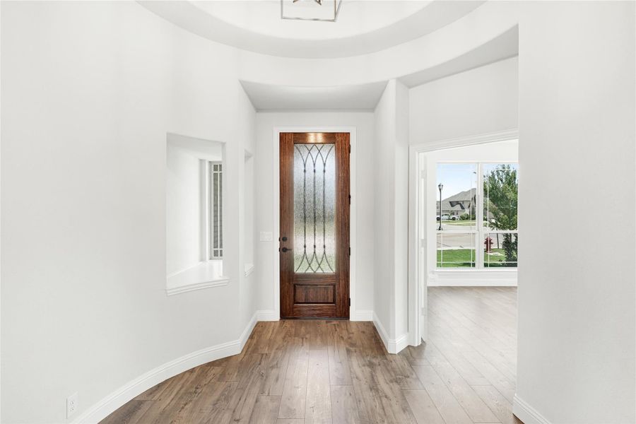 Home entryway with wood front door featuring decorative glass panel, hardwood floors, and tray ceiling