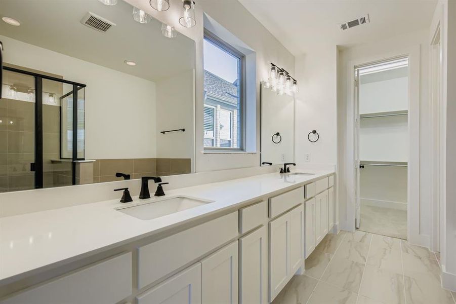 Full bath with a shower stall, double vanity, a spacious closet, and light marble finish flooring Full bath with a shower stall, double vanity, a spacious closet, and light marble finish flooring