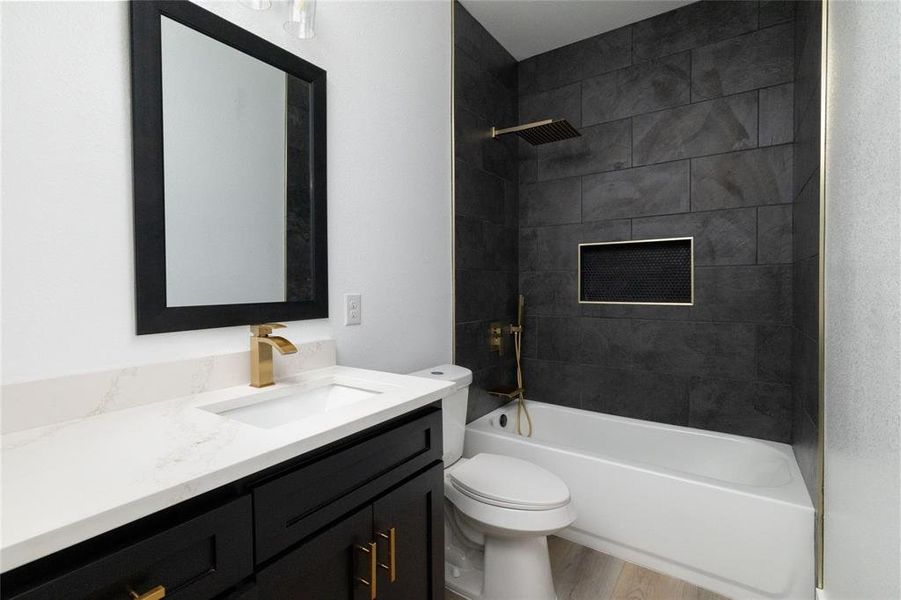 Full bathroom featuring hardwood / wood-style floors, tiled shower / bath combo, toilet, and vanity