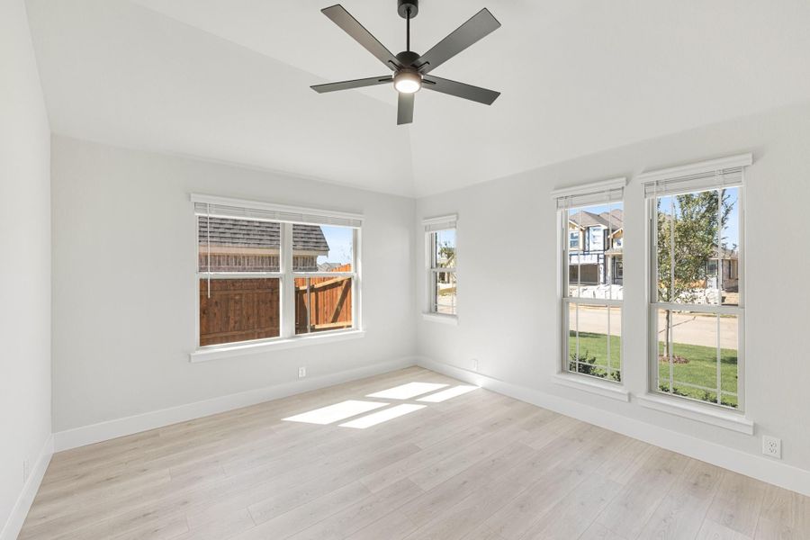 Empty bedroom with light wood floors, vaulted ceiling, ceiling fan, and multiple windows with natural light