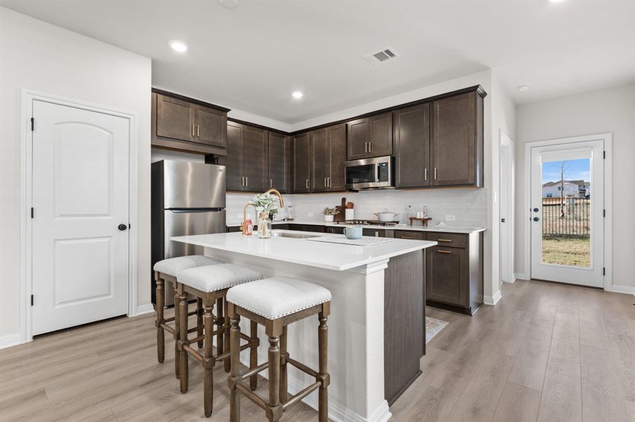 Kitchen with dark brown cabinetry, a breakfast bar area, stainless steel appliances, a kitchen island with sink, and light wood-style floors Kitchen with dark brown cabinetry, a breakfast bar area, stainless steel appliances, a kitchen island with sink, and light wood-style floors