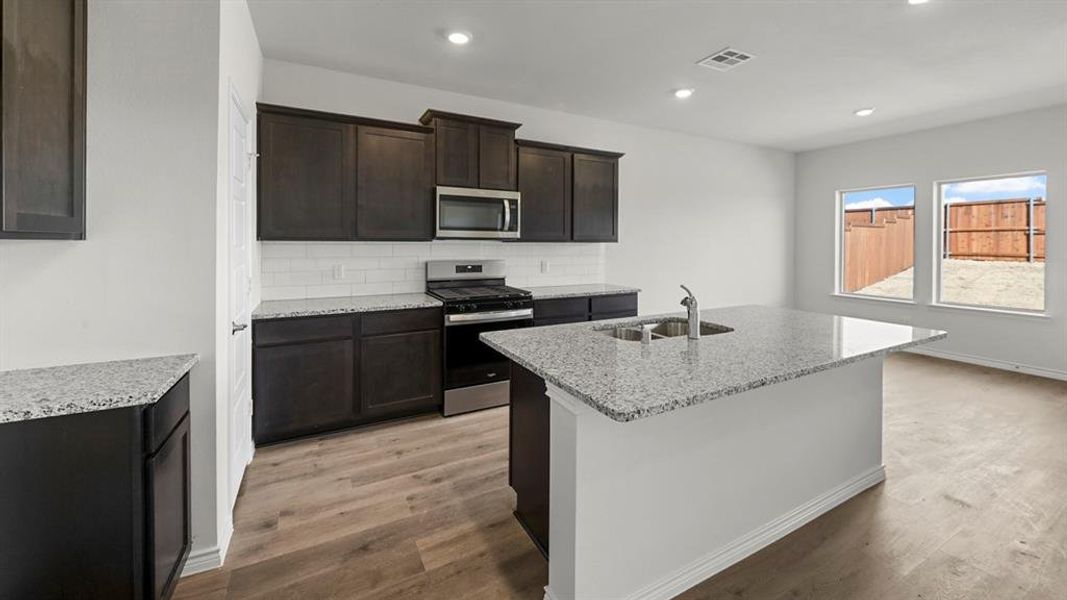 Kitchen featuring dark wood-finish cabinetry, light-toned granite countertops, and a subway tile backsplash