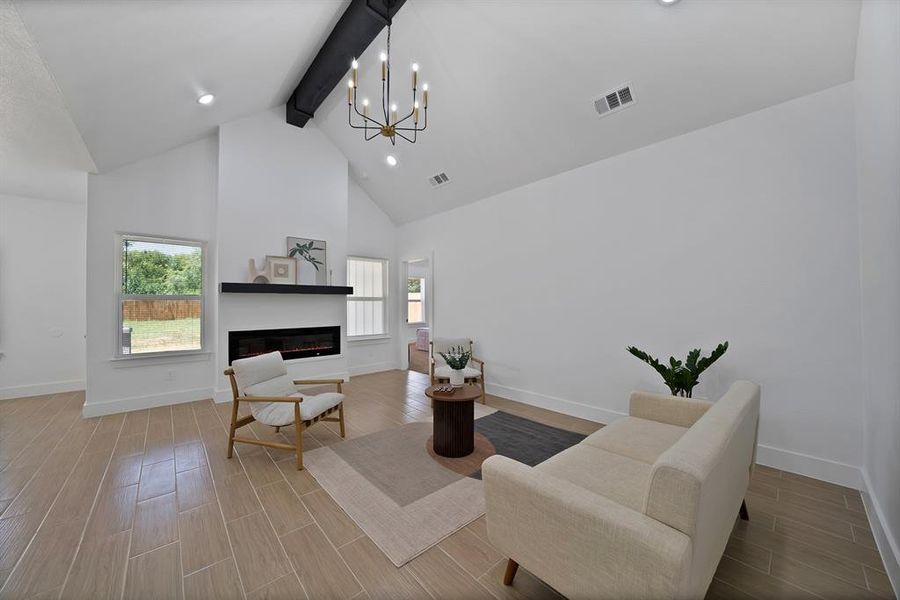 Living area featuring beam ceiling, high vaulted ceiling, healthy amount of natural light, wood tiled floors, and a glass covered fireplace