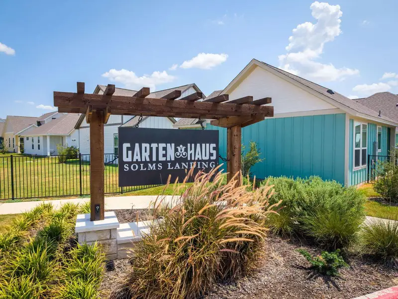A welcoming neighborhood sign stands amid landscaped beds before modern coastal-inspired residences. A welcoming neighborhood sign stands amid landscaped beds before modern coastal-inspired residences.