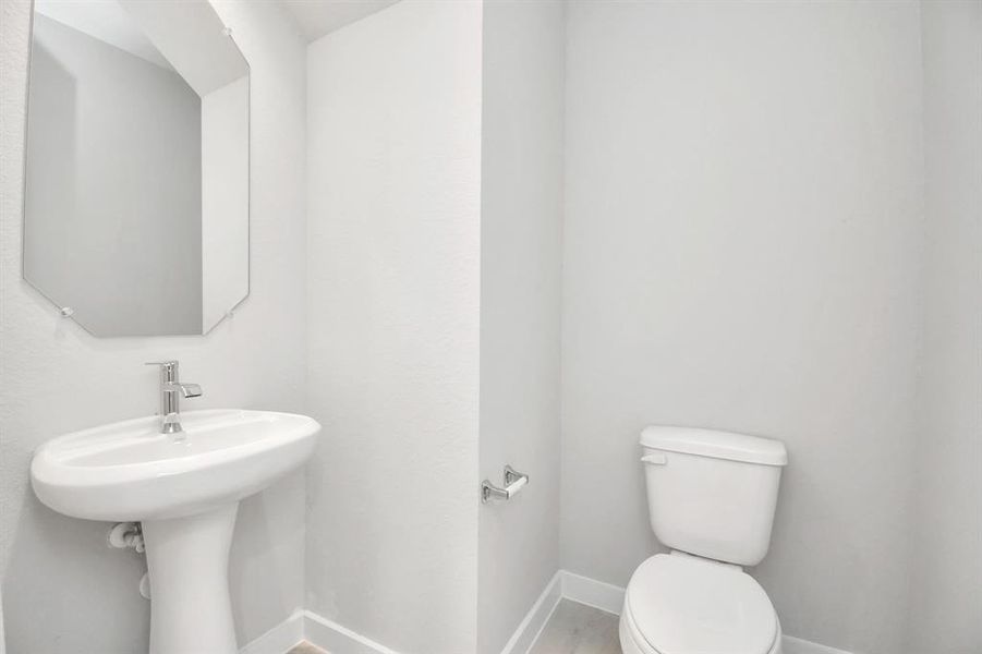 This half bathroom features a stylish pedestal sink, modern hardware, and bright recessed lighting, creating a sleek and inviting space. Example photo of completed home with similar plan. Actual may vary.