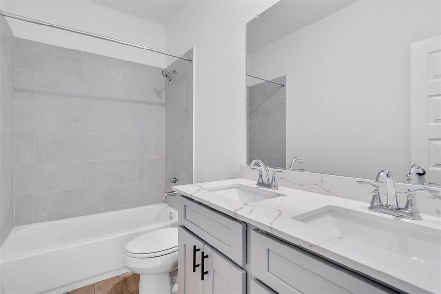 Secondary bath features tile flooring, bath/shower combo with tile surround, stained wood cabinets, beautiful light countertops, dual vanities, mirror, sleek fixtures and modern finishes.