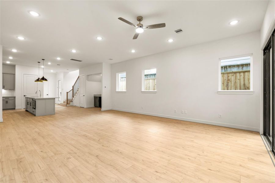 Generous living hall perspective — bright neutral walls, side-yard accent windows, and clear sightlines to the stairwell and kitchen hub.