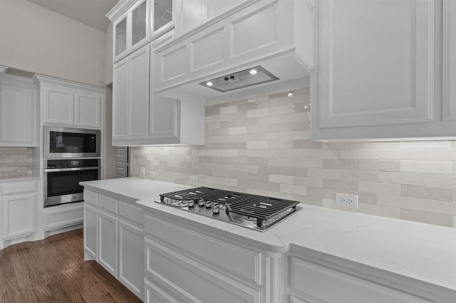 Kitchen featuring stainless steel appliances, light stone countertops, premium range hood, and white cabinets  Not actual home. Previous built example.