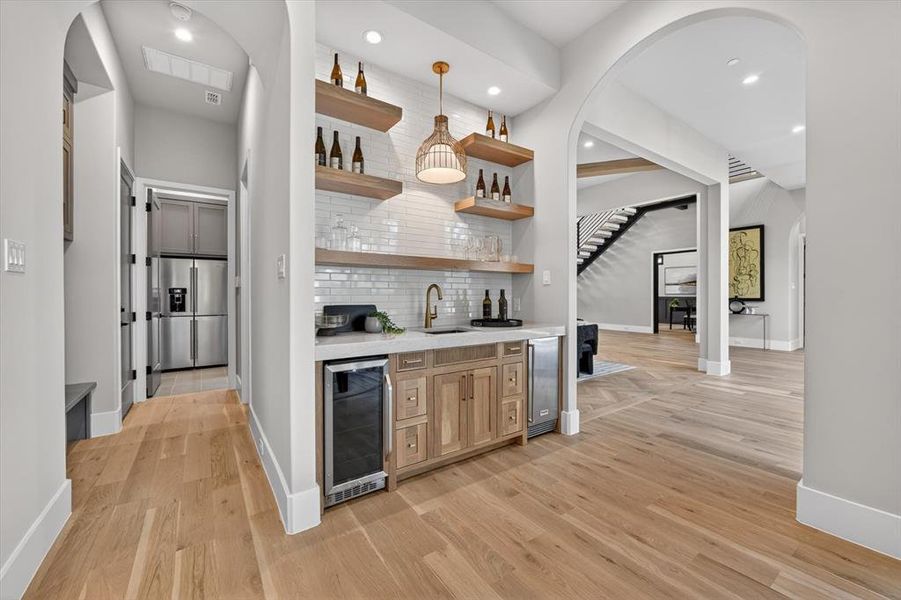 Built-in wet bar with wood-finish floating shelves, white subway tile backsplash, and an under-counter beverage cooler Built-in wet bar with wood-finish floating shelves, white subway tile backsplash, and an under-counter beverage cooler