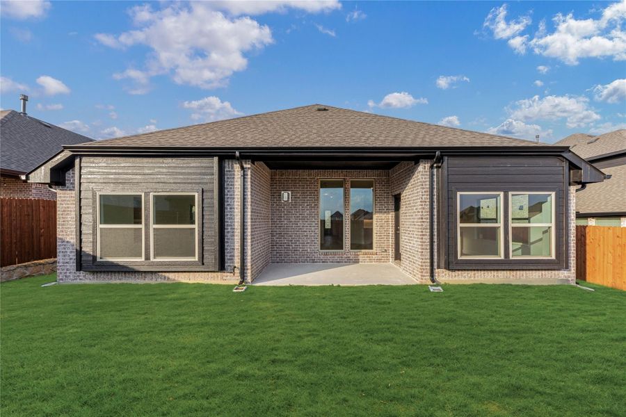 Single-story home rear exterior with brick and dark siding, covered patio, and green backyard lawn.