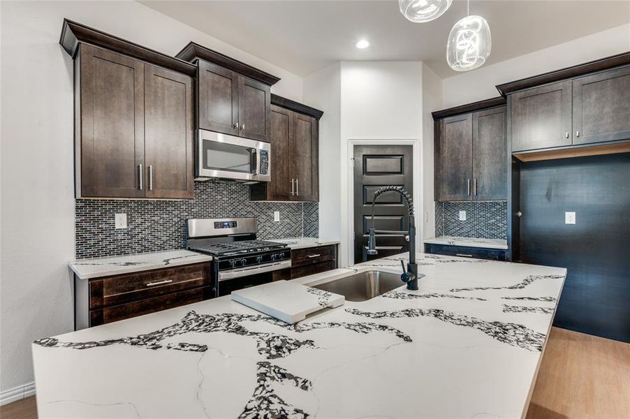 Kitchen featuring light hardwood / wood-style flooring, stainless steel appliances, light stone countertops, and hanging light fixtures