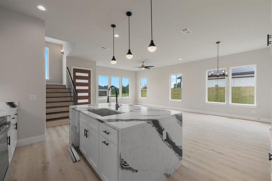 Kitchen featuring a sink, light wood-style flooring, white cabinetry, hanging light fixtures, and light stone countertops