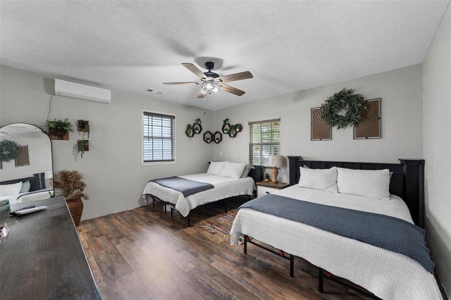 Bedroom with a wall unit AC, wood finished floors, a ceiling fan, and a textured ceiling Bedroom with a wall unit AC, wood finished floors, a ceiling fan, and a textured ceiling