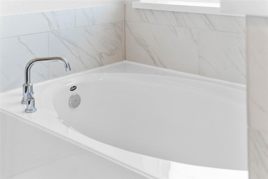 The photo showcases a luxurious built-in soaking tub, creating a spa-like retreat within the bathroom. The tub is set within a clean, white deck and surrounded by elegant white marble-look tile, perfect for unwinding after a long day.