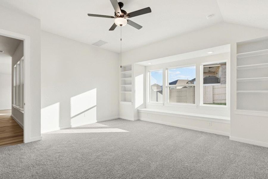Empty room featuring built in shelves, light carpet, and a ceiling fan Empty room featuring built in shelves, light carpet, and a ceiling fan