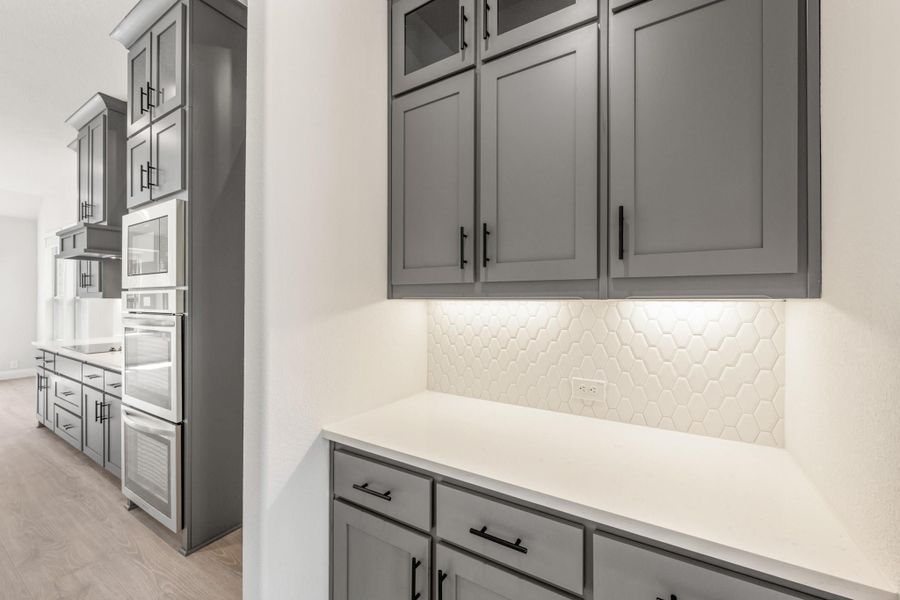 Kitchen with gray shaker cabinets, white quartz countertops, hexagon tile backsplash, and built-in double wall ovens