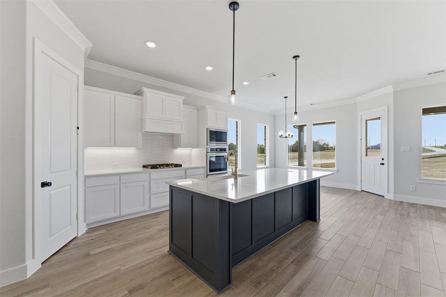Dual tone kitchen featuring dual tone cabinetry, light wood-type flooring, tasteful backsplash, an island with sink, and stainless steel appliances