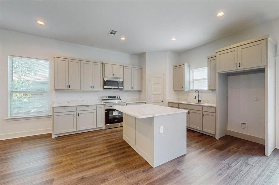 Kitchen with dark hardwood / wood-style flooring, a center island, light stone countertops, electric range oven, and sink