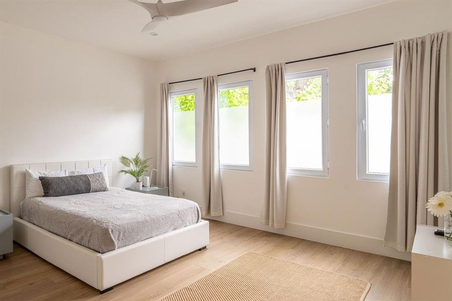 Bedroom with light hardwood / wood-style flooring, ceiling fan, and multiple windows Bedroom with light hardwood / wood-style flooring, ceiling fan, and multiple windows