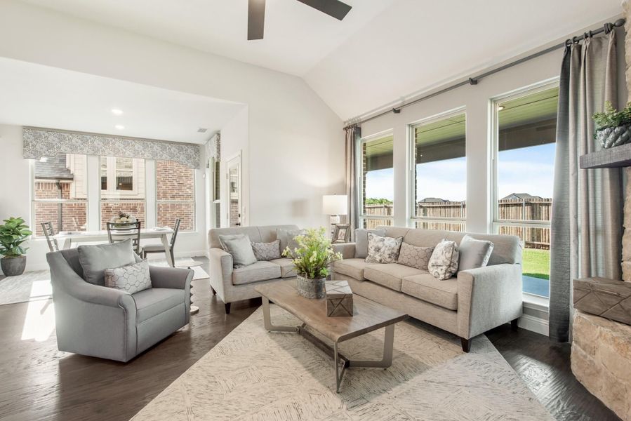 Living room with vaulted ceiling, gray sofas, hardwood floors, and large windows with backyard view