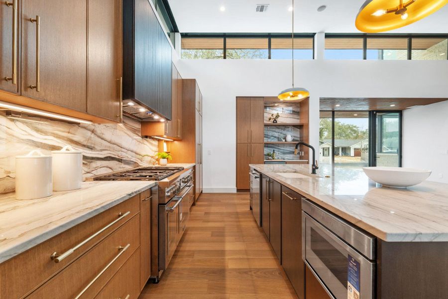 Dual tone kitchen with light stone counters, stainless steel appliances, a large island, light wood-style flooring, and pendant lighting