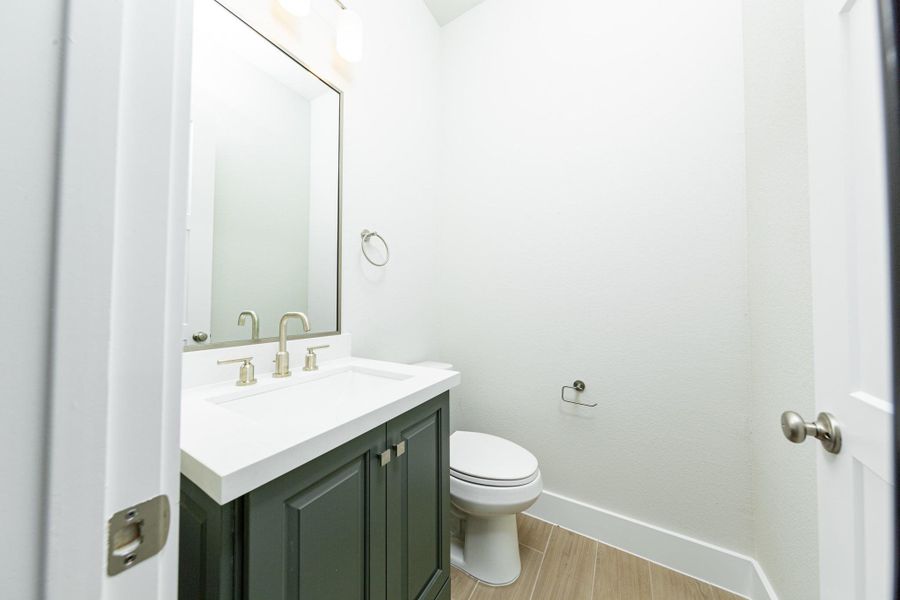 The powder room offers convenience and a modern aesthetic. It features a stained cabinet with quartz countertop and brushed nickel fixtures, matching wall-mounted towel ring, and a simple, large rectangular mirror. The powder room offers convenience and a modern aesthetic. It features a stained cabinet with quartz countertop and brushed nickel fixtures, matching wall-mounted towel ring, and a simple, large rectangular mirror.
