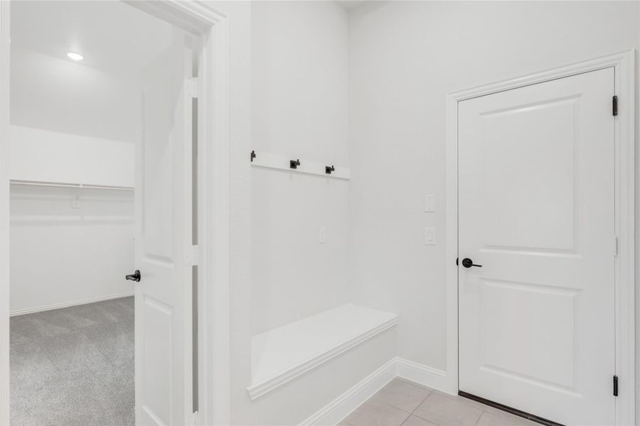 Mudroom with built-in bench, wall hooks, and white doors leading to a carpeted walk-in closet Mudroom with built-in bench, wall hooks, and white doors leading to a carpeted walk-in closet