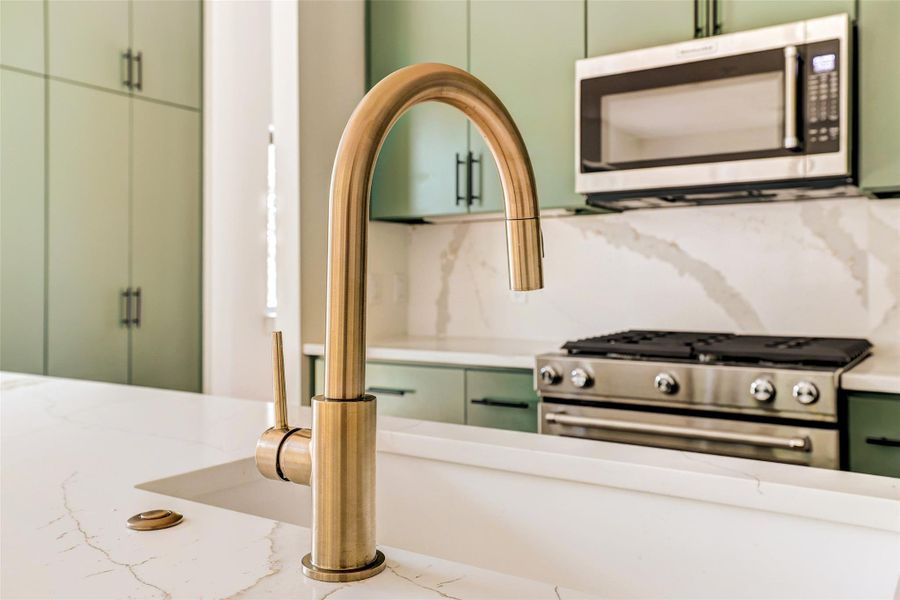 Kitchen featuring stainless steel appliances, green cabinetry, light stone counters, and backsplash