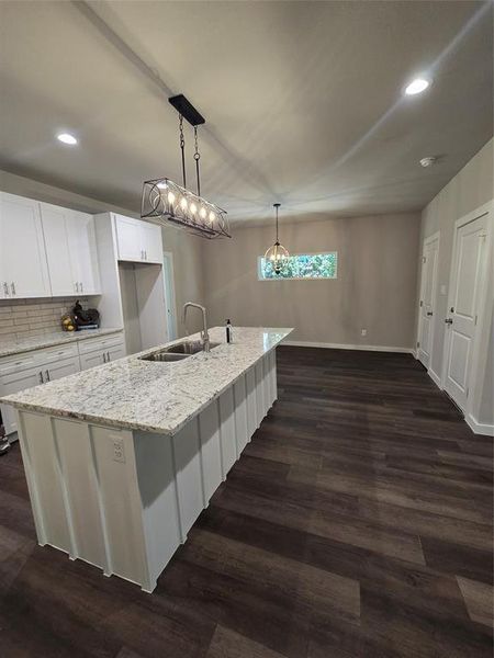 Kitchen featuring white cabinets, dark hardwood / wood-style flooring, decorative light fixtures, a kitchen island with sink, and sink