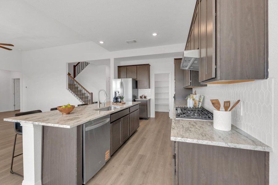 Kitchen featuring backsplash, light wood-style floors, light stone counters, an island with sink, and stainless steel appliances Kitchen featuring backsplash, light wood-style floors, light stone counters, an island with sink, and stainless steel appliances