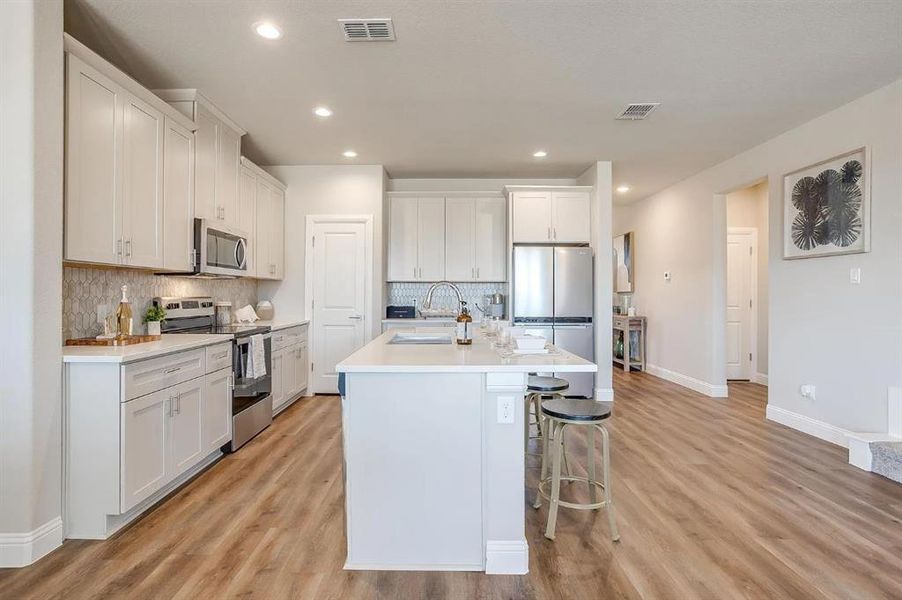 Kitchen with white cabinetry, sink, an island with sink, and appliances with stainless steel finishes