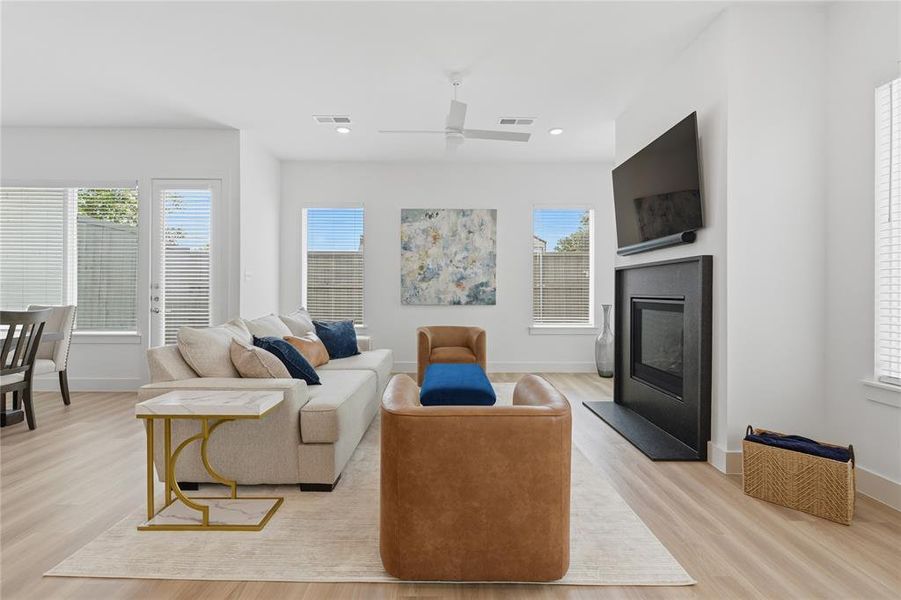 Open-concept living area featuring light wood-finish flooring, white walls, and a modern fireplace with a dark surround