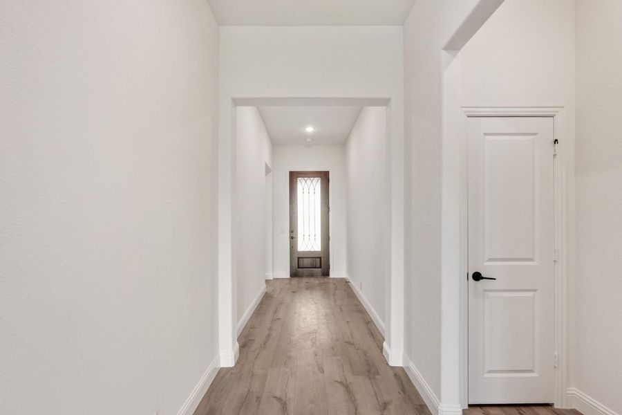 Hallway with white walls, wood-look floors, and decorative glass front door at the end Hallway with white walls, wood-look floors, and decorative glass front door at the end