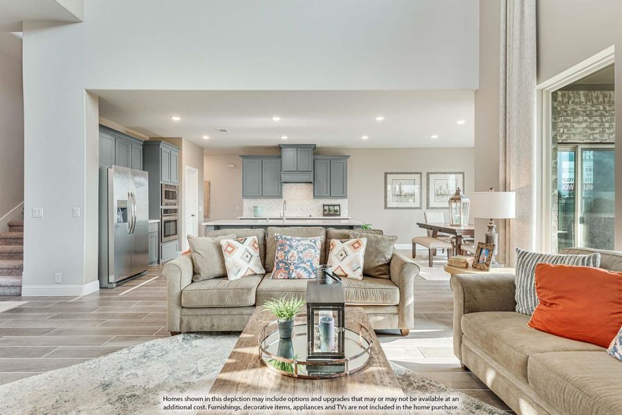 Open-concept living room with neutral sofas and glass coffee table, open to kitchen with gray cabinets and tile floors