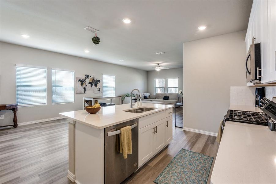 Kitchen featuring white cabinets, open floor plan, stainless steel appliances, light wood-style flooring, and an island with sink