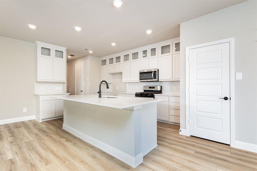Kitchen with white cabinetry, gas range, stainless steel microwave, a center island with sink, and recessed lighting