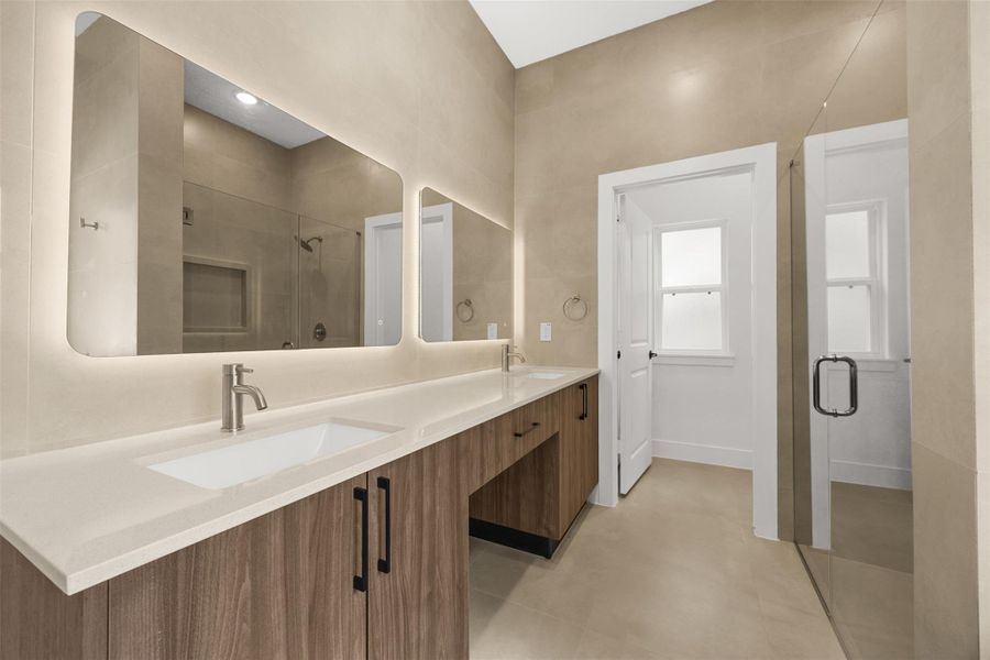 Dual-sink vanity with quartz countertops, custom designed cabinetry, and illuminated mirrors.