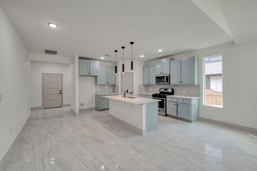 Kitchen with a kitchen breakfast bar, backsplash, appliances with stainless steel finishes, a center island with seating and sink, and pendant lighting Kitchen with a kitchen breakfast bar, backsplash, appliances with stainless steel finishes, a center island with seating and sink, and pendant lighting